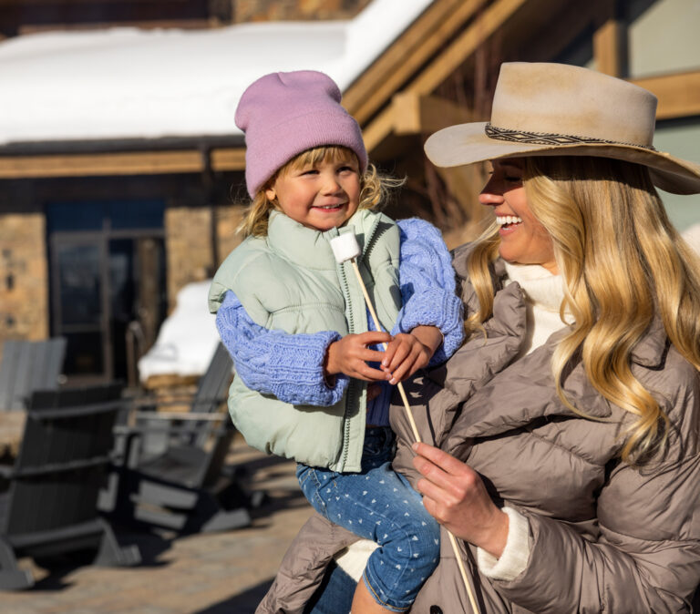 mom holding little girl with a marshmallow on a stick.