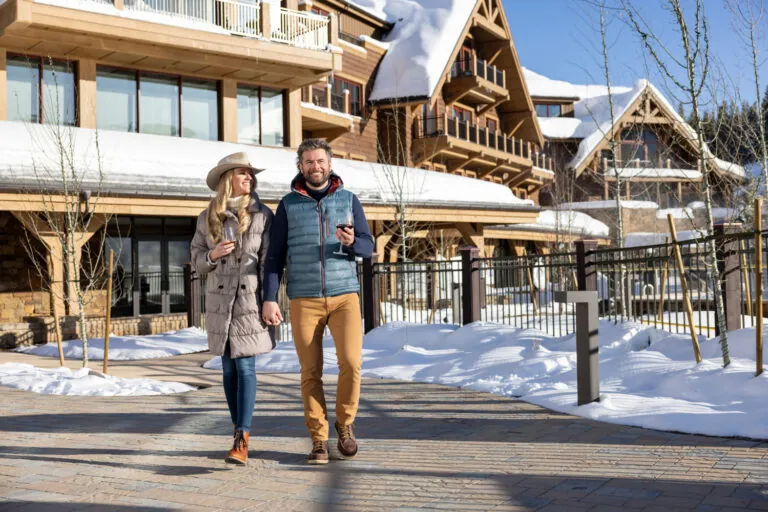 A couple walking around the resort with glasses of wine in the winter.