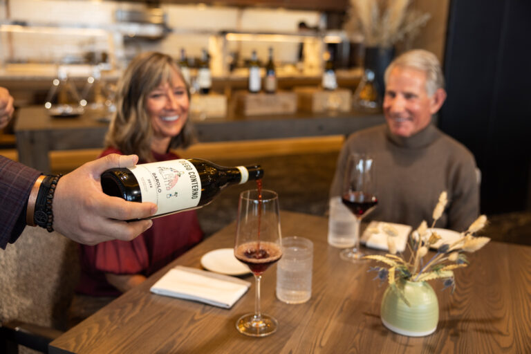 A couple dining while being poured a glass of wine.