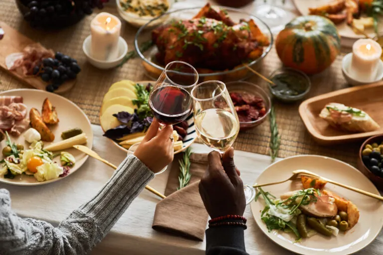 Close up of two people toasting with wine glasses at festive dinner table celebrating Thanksgiving.
