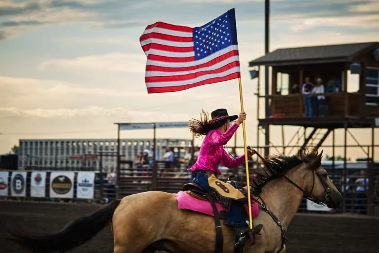 A woman riding a horse with the American Flag.
