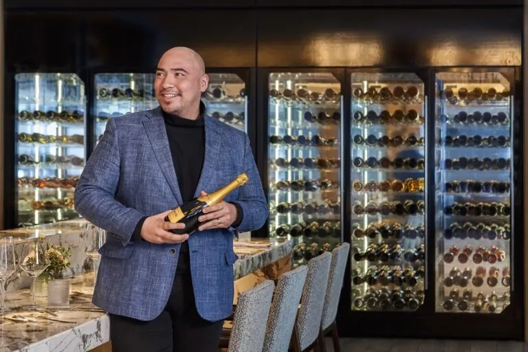 Oscar Chinchilla with a bottle of champagne standing in front of a wine cellar