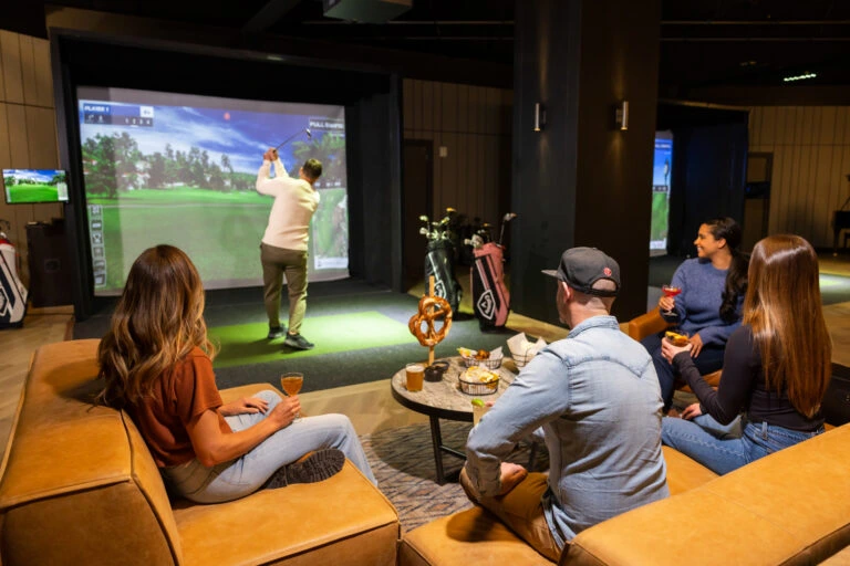 A group of friends enjoying food and virtual golf simulator at the Rivalry Room