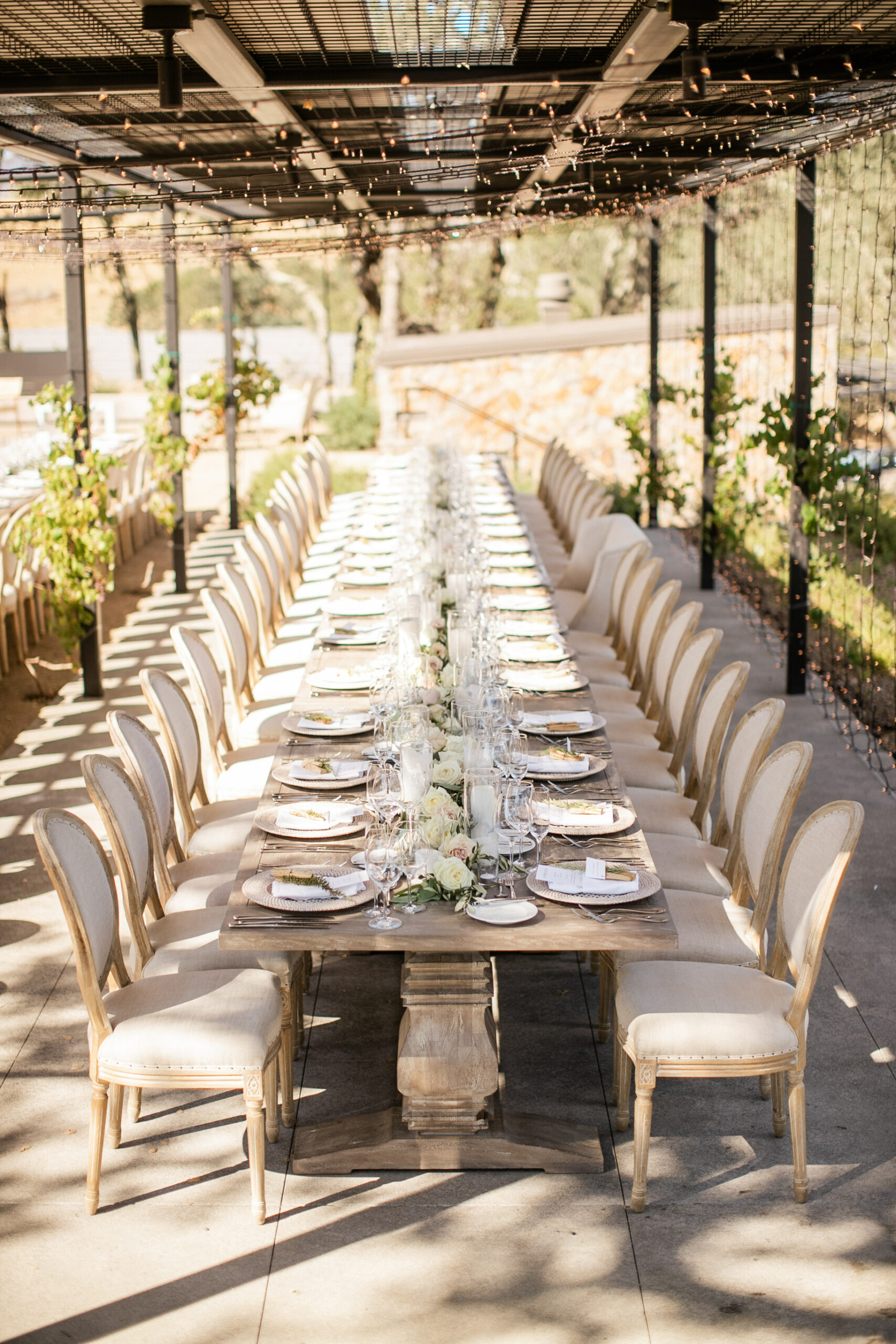 long wood table with cream chairs under string lights