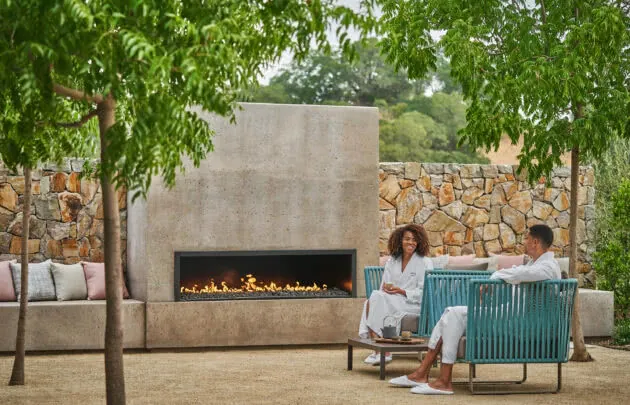 A couple wearing white robes sitting in blue chairs in front of fireplace