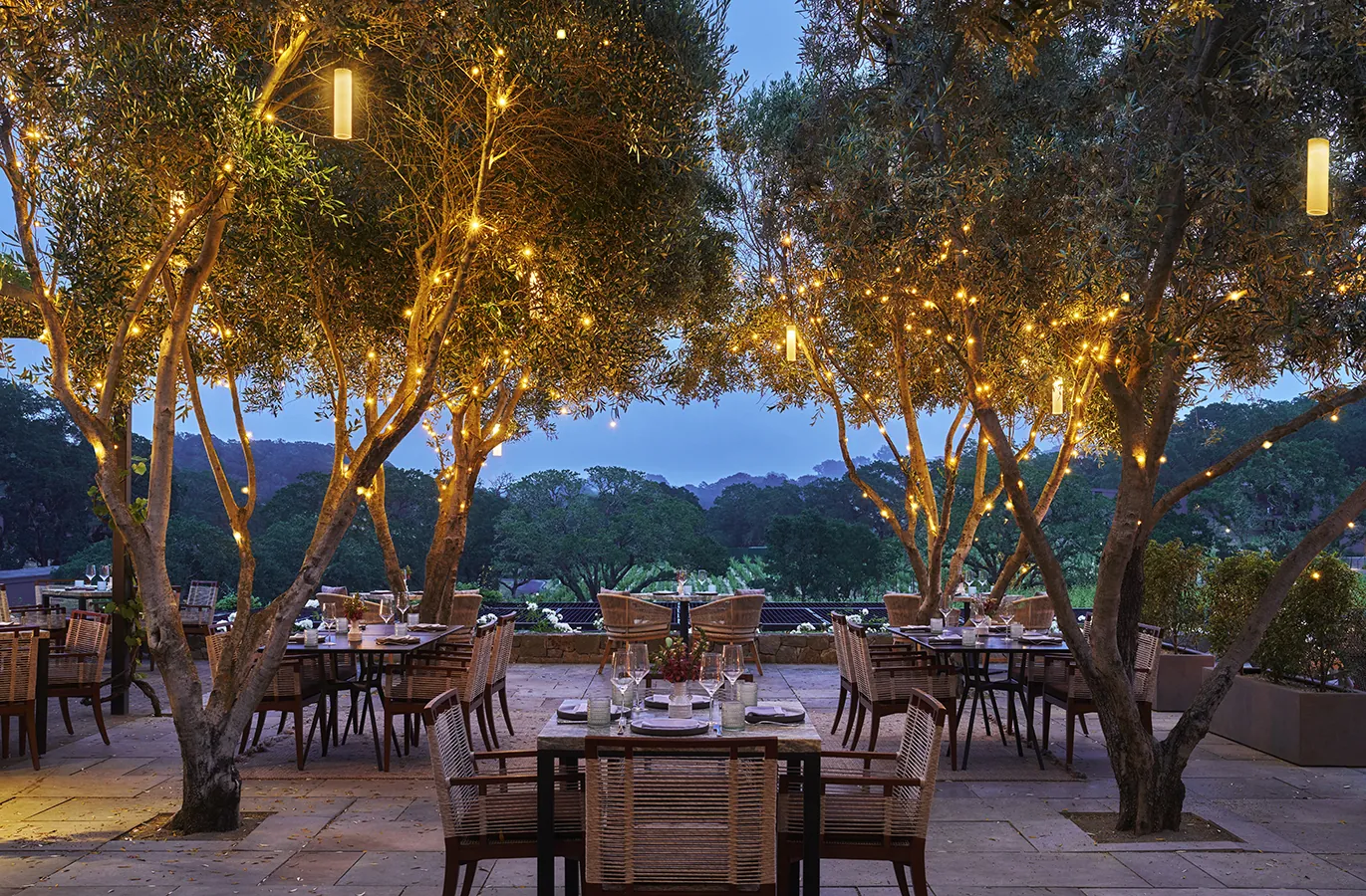 Hazel Hill dining terrace with tables set and twinkle lights in trees.