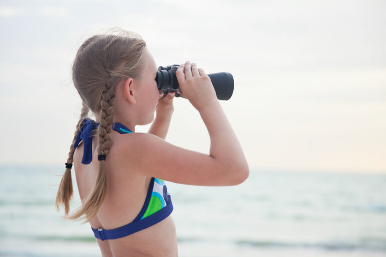 Young girl looking at the ocean through binoculars