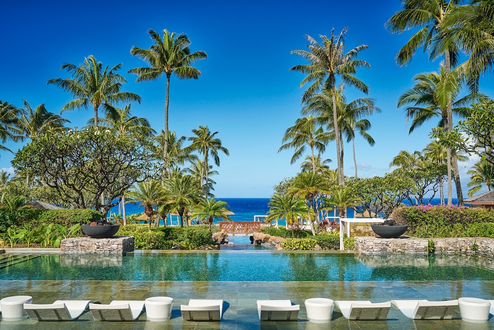 Resort pool surrounded by palm trees and ocean view
