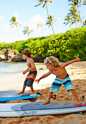 Two kids getting ready to surf at Montage Kapalua Bay.