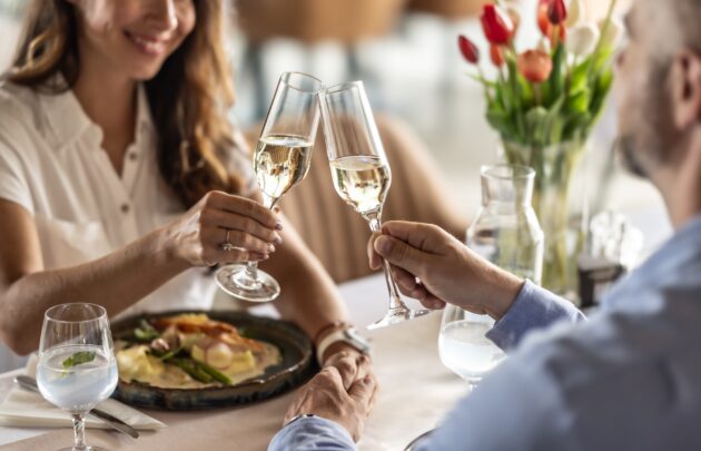 A couple in love is enjoying a romantic dinner at a restaurant and toasting with champagne or prosecco - close up