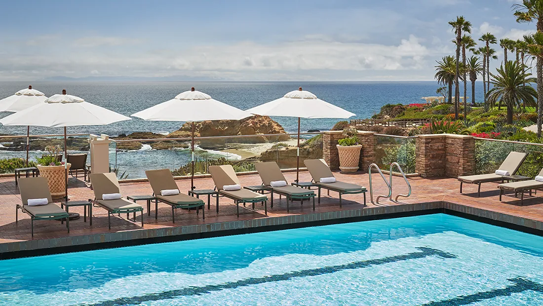Pool at Montage Laguna Beach resort with lounge chairs and umbrellas set up, with ocean views