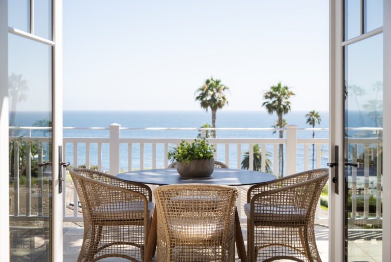Patio table with wicker chairs overlooking the ocean and palm trees.