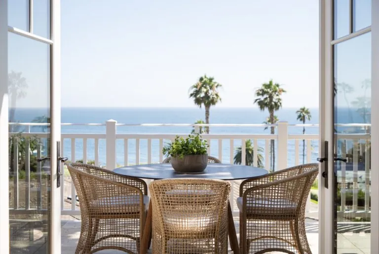 Patio table with wicker chairs overlooking the ocean and palm trees.
