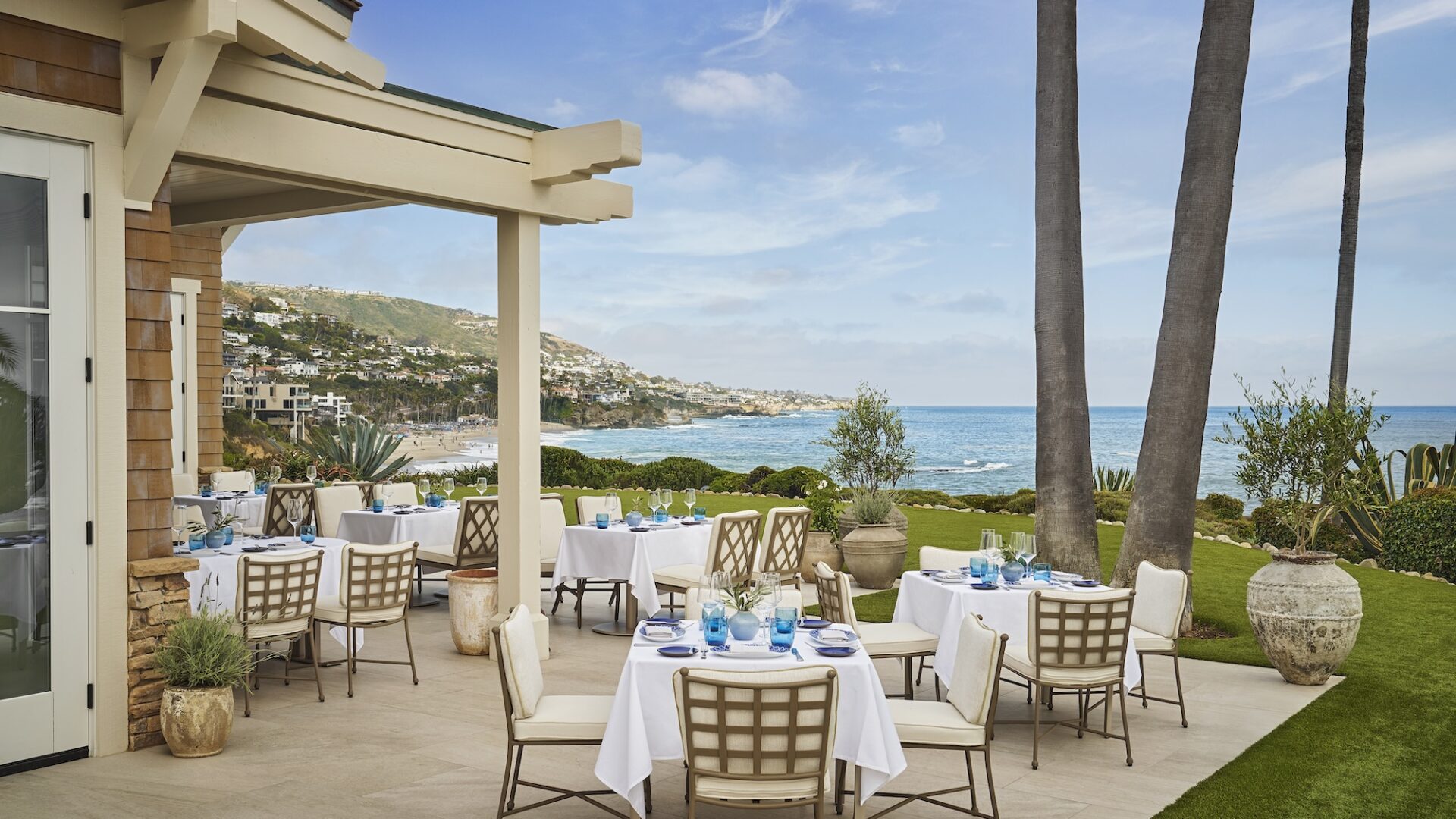 Outdoor seaside dining terrace with white tablecloths and ocean views.