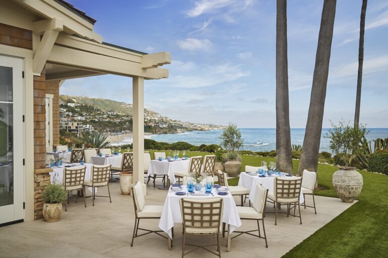 Outdoor seaside dining terrace with white tablecloths and ocean views.