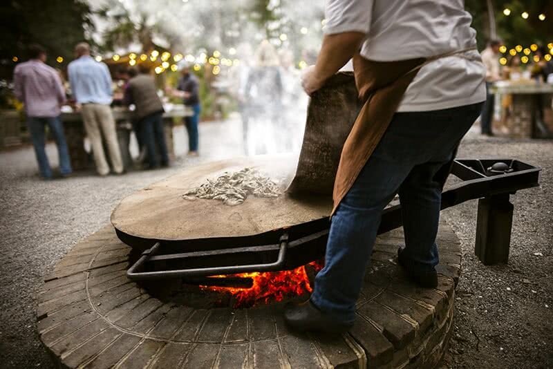 Chef roasting oysters on large wooden surface above fire