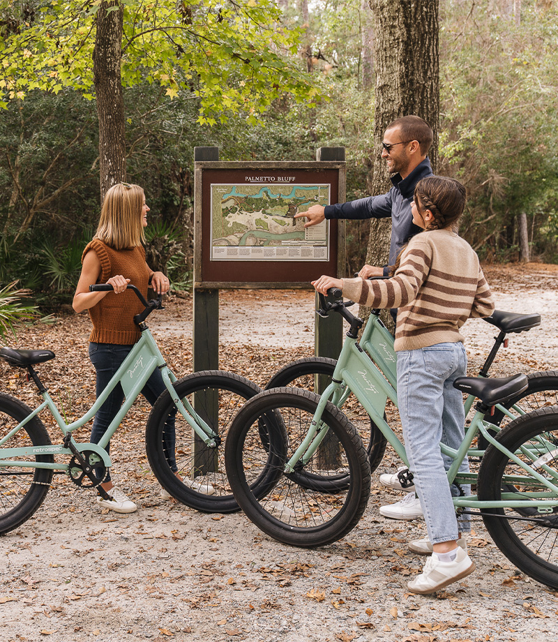 Three people on bikes looking at a map of Palmetto Bluff
