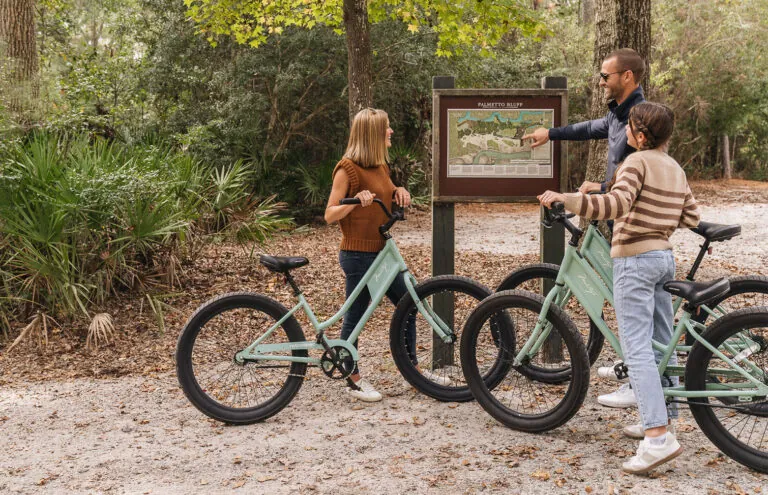 Three people on bikes looking at a map of Palmetto Bluff